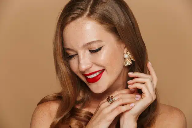 Close up of a beautiful young woman wearing makeup and jewelry accessories posing isolated over beige wall Premium Photo