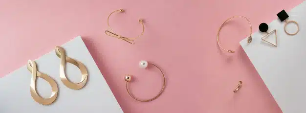 Panoramic top view of modern golden accessories with pearls on pink and white
