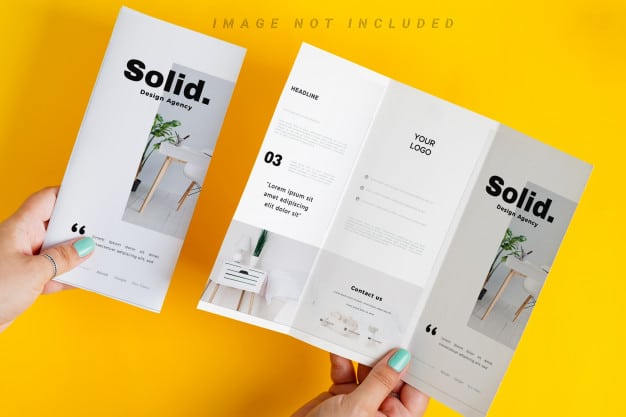 Woman's hands are holding mock-up brochure above yellow table Premium Psd
